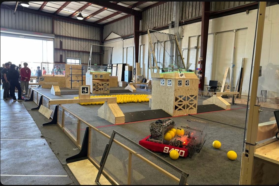 A regulation-size FRC practice field inside a warehouse, with plywood obstacles, rows of yellow game balls, and a red competition robot parked on the carpet.