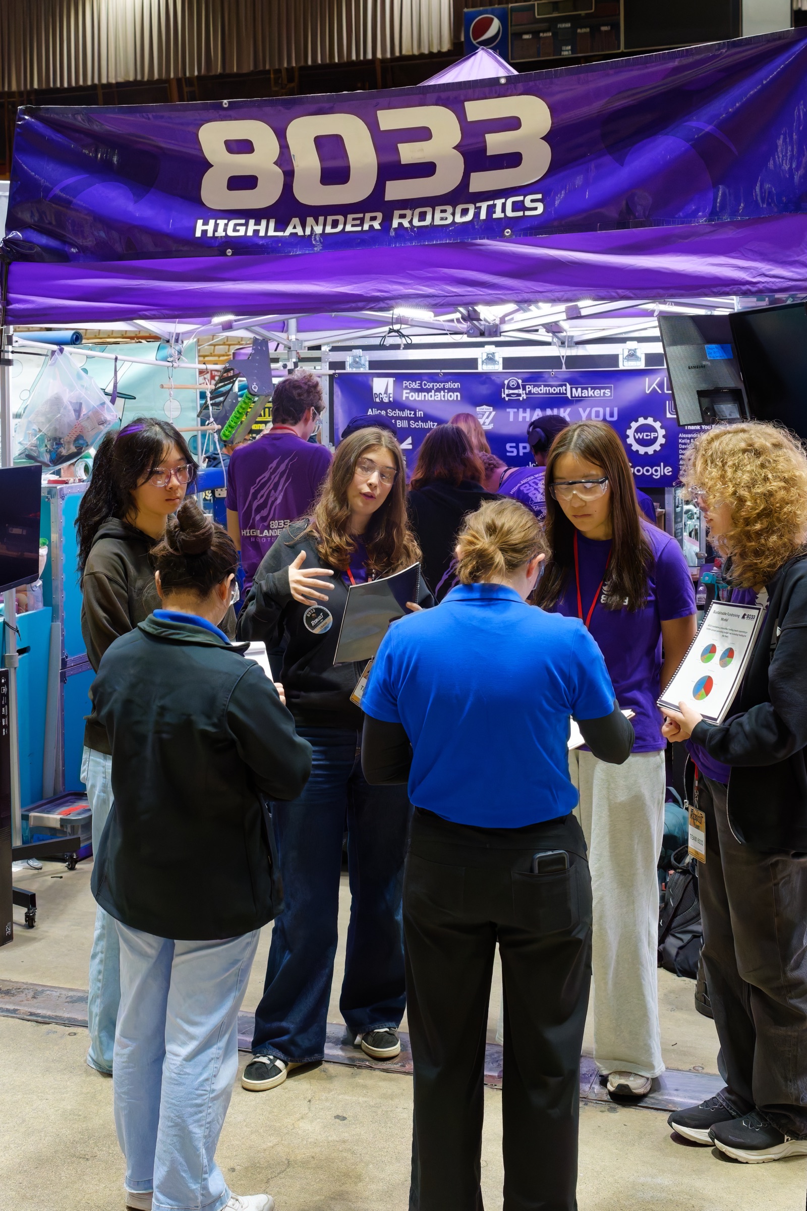 Four Highlander Robotics team ambassadors smiling for the camera in matching uniforms at a competition.