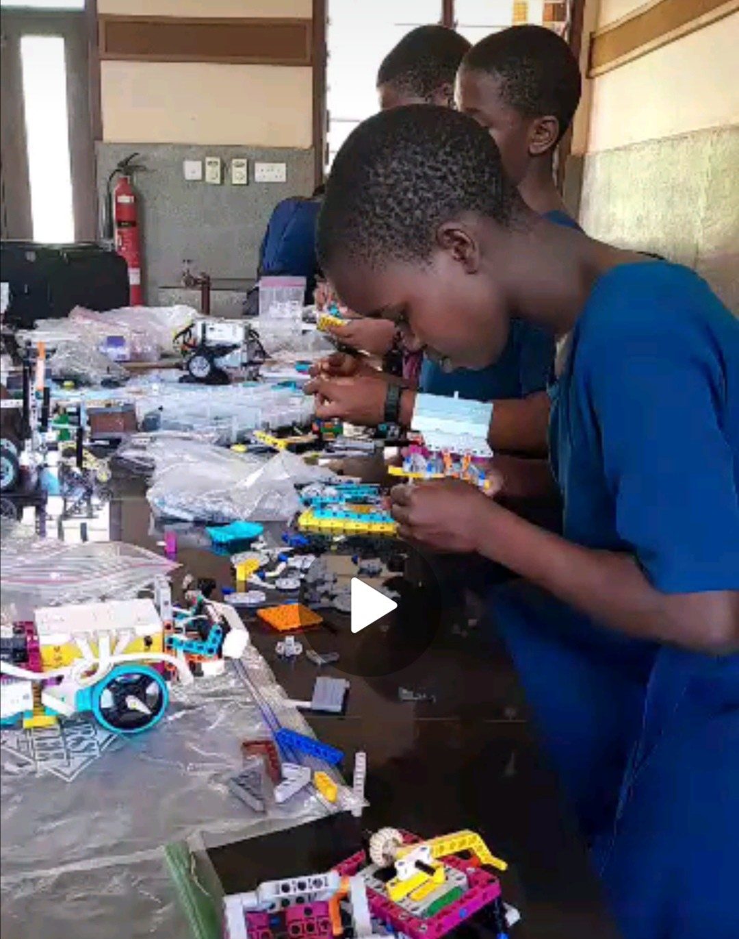 Students at SEGA Girls Secondary School in Tanzania lean over a table crowded with LEGO SPIKE robot parts, connecting pieces during a training session.
