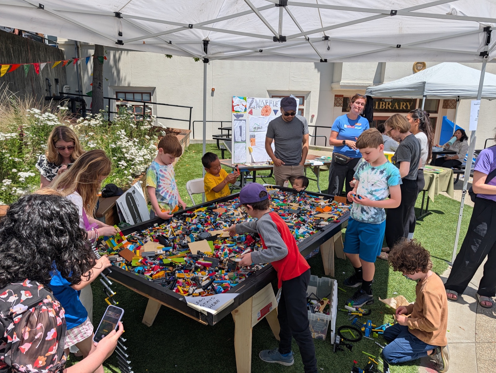 Kids and parents gathered around a large outdoor LEGO play table at the Piedmont School Maker Faire.