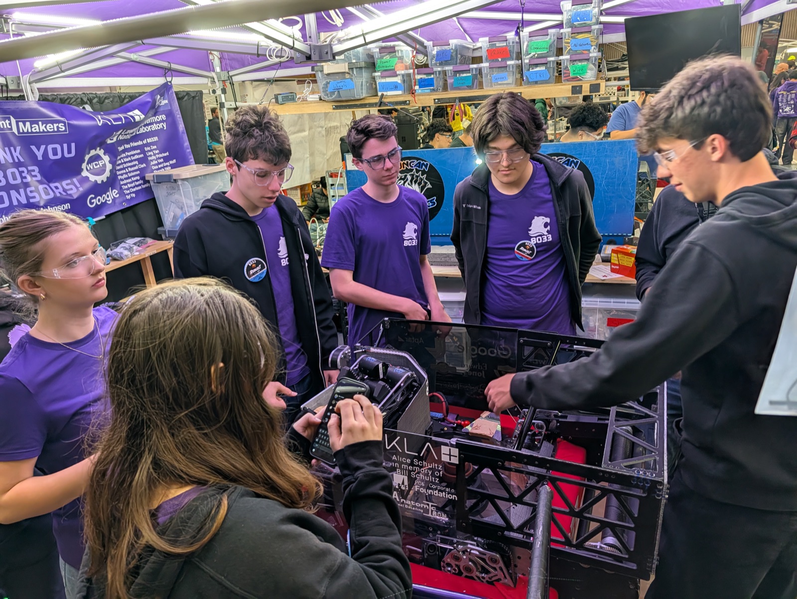 Members of Highlander Robotics Team 8033 around their robot at a championship pit, with sponsor banners visible.